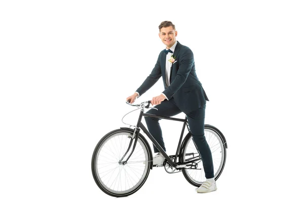 Joyeux beau marié en costume élégant et baskets assis sur vélo isolé sur blanc — Photo de stock