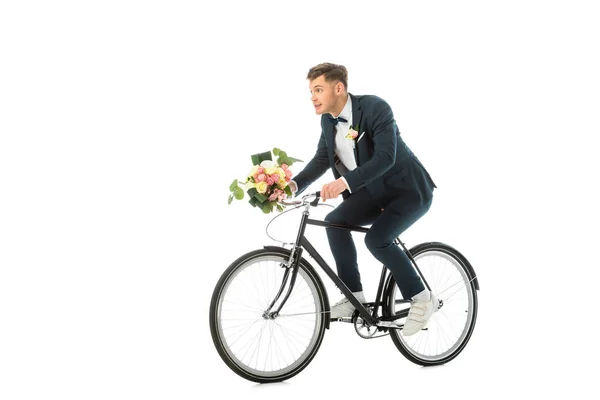 Fröhliche Bräutigam in Turnschuhen Fahrrad fahren und halten Hochzeitsstrauß isoliert auf weiß — Stockfoto
