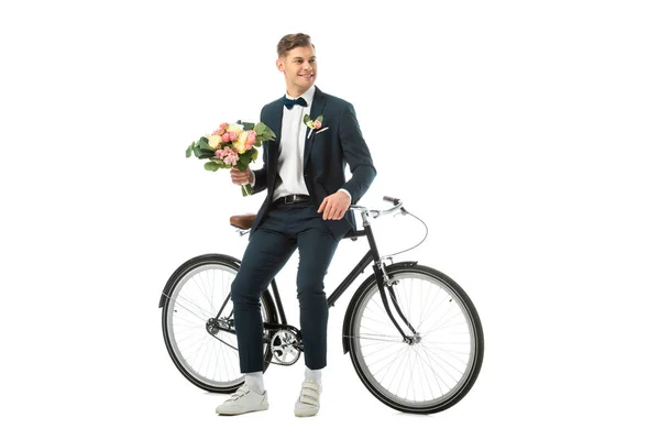 Cheerful groom holding wedding bouquet while standing near bike isolated on white — Stock Photo