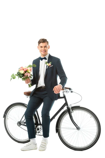Веселий наречений стоїть біля велосипеда і тримає весільний букет, дивлячись на камеру ізольовано на білому — стокове фото
