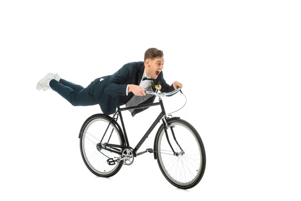 Novio excitado en traje elegante haciendo acrobacias en bicicleta aislado en blanco - foto de stock