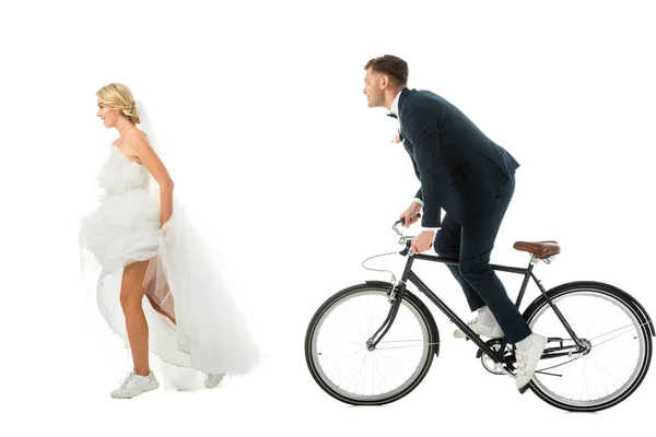 Noiva bonita em vestido de noiva correndo do noivo na bicicleta isolada no branco — Fotografia de Stock