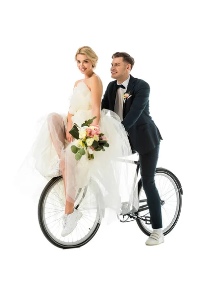 Beautiful bride holding wedding bouquet while sitting on bicycle together with groom isolated on white — Stock Photo
