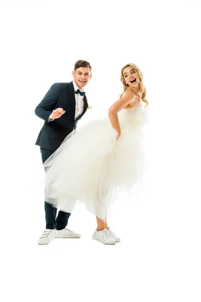 Allegro sposo e sposa ballare in abiti eleganti e scarpe da ginnastica isolate su bianco — Foto stock
