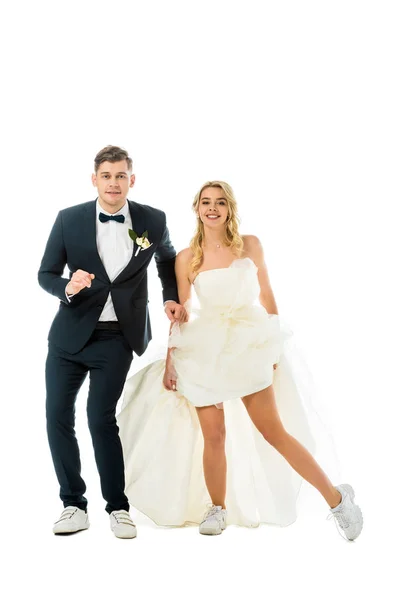 Happy groom and bride in elegant clothes and sneakers dancing while looking at camera isolated on white — Stock Photo