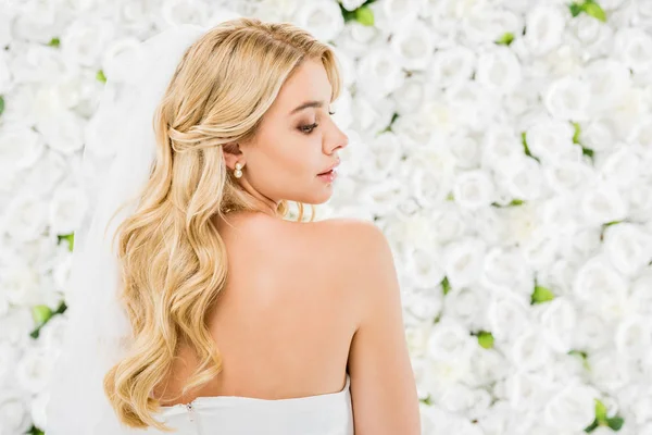 Attraktive junge Frau mit blonden Haaren posiert vor der Kamera auf weißem Blumenhintergrund — Stockfoto
