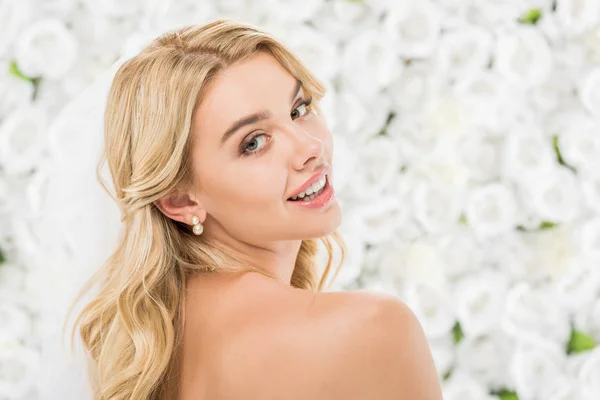 Hermosa chica desnuda con el pelo rubio posando en la cámara sobre fondo floral blanco - foto de stock