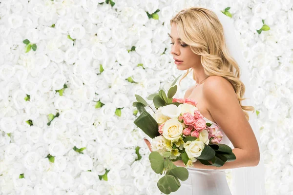 Schöne junge Braut hält Brautstrauß auf weißem Blumenhintergrund — Stockfoto