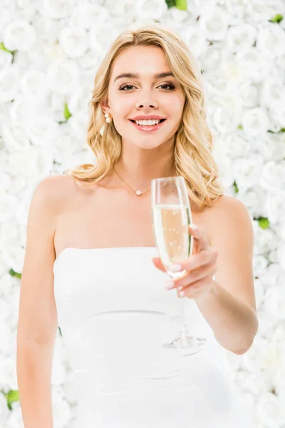 Selektiver Fokus attraktiver junger Frau mit einem Glas Champagner auf weißem floralem Hintergrund — Stockfoto