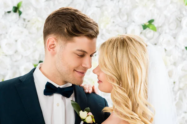 Heureux jeune marié et mariée debout face à face sur fond floral blanc — Photo de stock