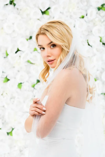Heureuse belle mariée regardant caméra sur fond floral blanc — Photo de stock
