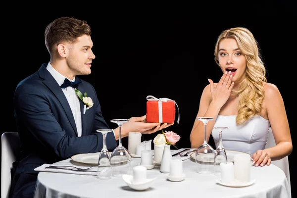 Sorrindo jovem noivo apresentando caixa de presente vermelho para noiva surpresa isolado em preto — Fotografia de Stock