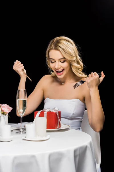 Noiva alegre com garfo e faca imitando comer com caixa de presente isolado em preto — Fotografia de Stock