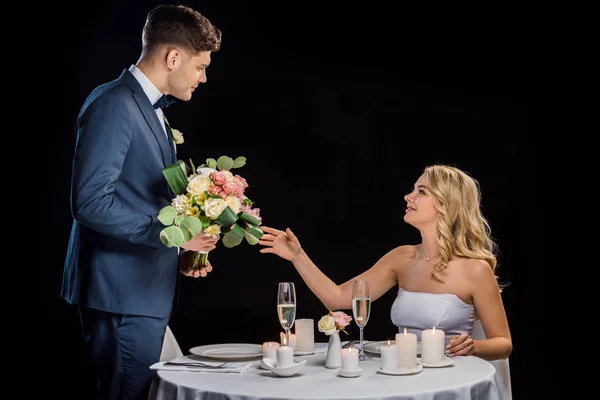 Bello sposo presentando bouquet da sposa a bella sposa isolata su nero — Foto stock