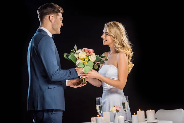 Lächelnder Bräutigam überreicht Hochzeitsstrauß an glückliche Braut isoliert auf Schwarz — Stockfoto