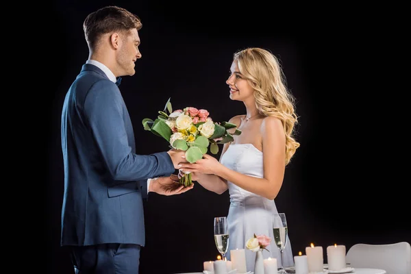 Novio sonriente presentando ramo de boda a novia feliz aislado en negro - foto de stock