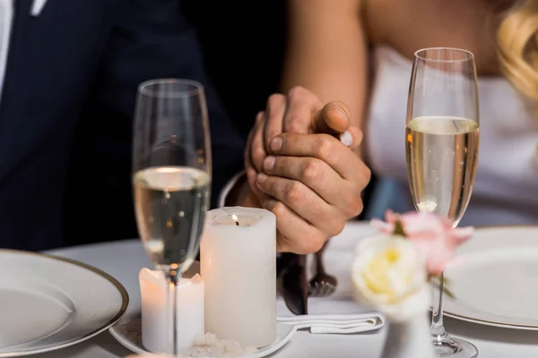 Enfoque selectivo del hombre y la mujer tomados de la mano mientras están sentados en la mesa servida sobre fondo negro - foto de stock