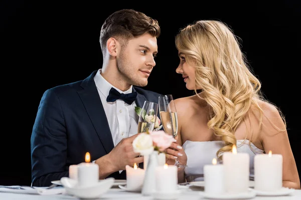 Novio sonriente y novia tintineando copas de champán y mirándose aislados en negro - foto de stock