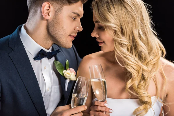 Happy couple sitting face to face and clinking glasses of champagne isolated on black — Stock Photo