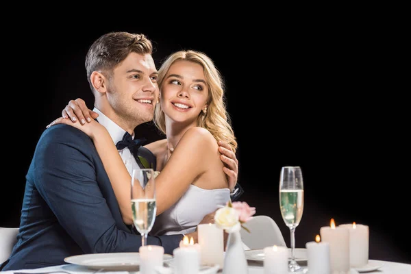 Novio feliz y novia abrazando mientras está sentado en la mesa servida aislado en negro — Stock Photo