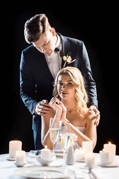 Schöner Bräutigam umarmt verträumte Braut von hinten an den Schultern isoliert auf schwarz — Stockfoto