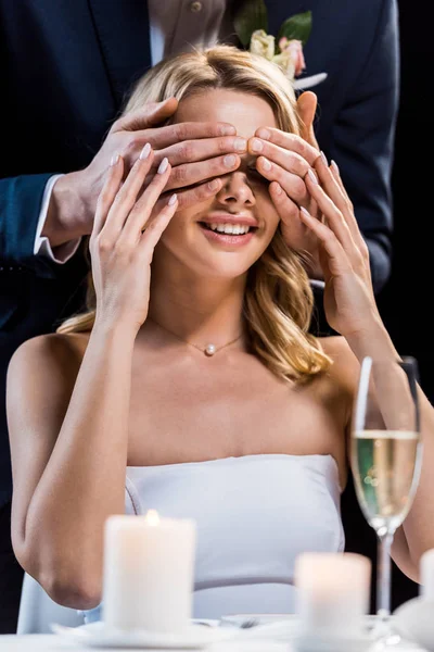 Foco selectivo de novia feliz con los ojos cerrados por los novios manos aisladas en negro - foto de stock