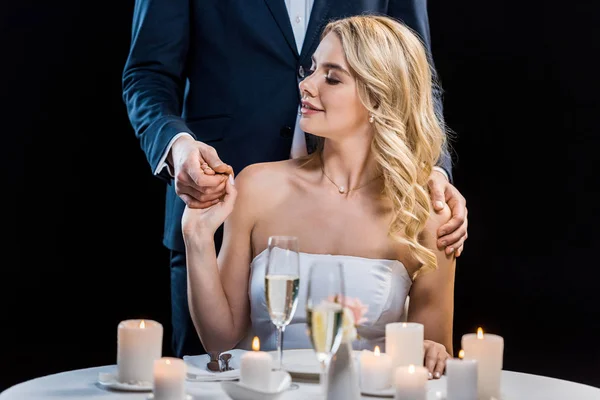 Teilansicht des Bräutigams, der hinter der sitzenden Braut steht und ihre Schultern isoliert auf schwarz umarmt — Stockfoto