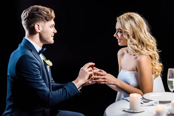 Guapo joven hombre haciendo matrimonio propuesta a feliz joven mujer aislado en negro - foto de stock