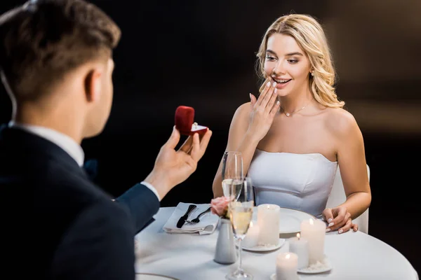 Enfoque selectivo del hombre haciendo propuesta de matrimonio a la mujer divertida sobre fondo negro - foto de stock