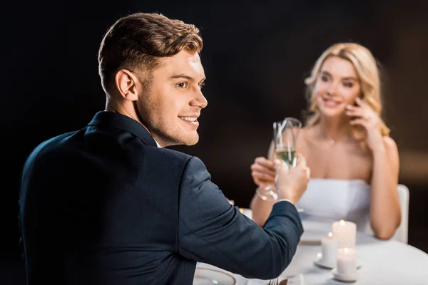 Selektiver Fokus des hübschen Bräutigams und der schönen Braut, die Champagnergläser auf schwarzem Hintergrund klimpert — Stockfoto