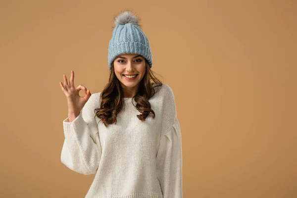 Felice sorridente ragazza in maglia cappello mostrando segno ok isolato su beige — Foto stock