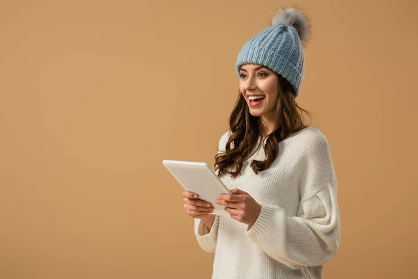 Stunning curly girl in knitted hat holding digital tablet and laughing isolated on beige — Stock Photo