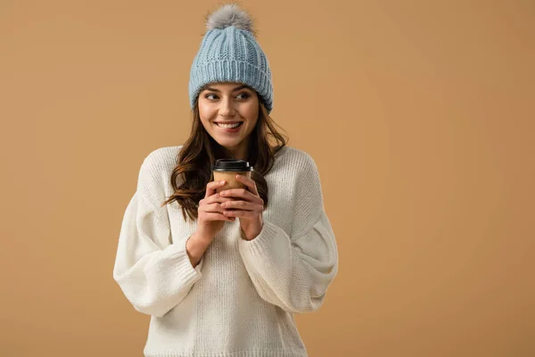 Fröhliches Mädchen mit Strickmütze, Kaffeetasse in der Hand und isoliert lächelnd auf beige — Stockfoto