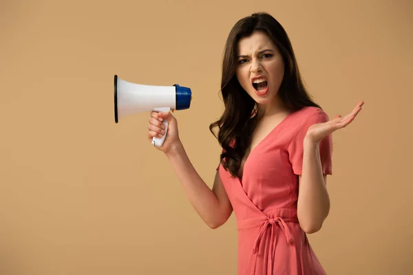 Angry brunette woman in dress holding megaphone and screaming isolated on beige — Stock Photo