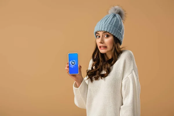 Confused young woman holding smartphone with shazam app on screen isolated on beige — Stock Photo