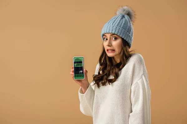 Confundido hermosa chica sosteniendo teléfono inteligente con aplicación de reserva en la pantalla aislada en beige - foto de stock