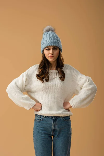 Skeptical brunette girl in white sweater standing with arms akimbo isolated on beige — Stock Photo