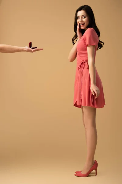 Cropped view of man making marriage proposal to surprised brunette girl in dress on beige background — Stock Photo