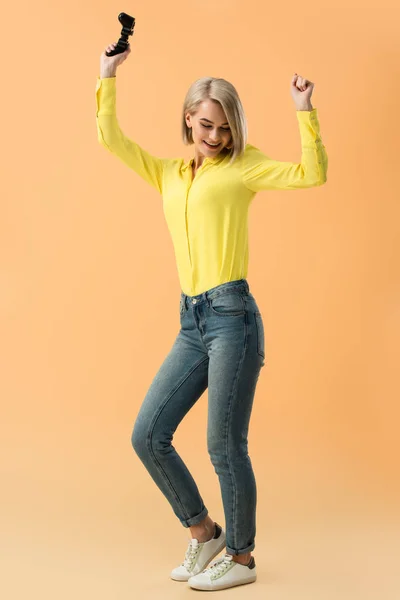 Улыбающаяся блондинка держит джойстик и танцует на оранжевом фоне — стоковое фото