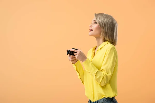 Мечтательная молодая женщина в желтой рубашке держит джойстик и смотрит вверх изолированы на оранжевый — стоковое фото