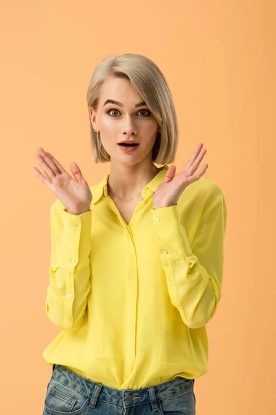 Mujer hermosa sorprendida en camisa amarilla mirando a la cámara aislada en naranja - foto de stock