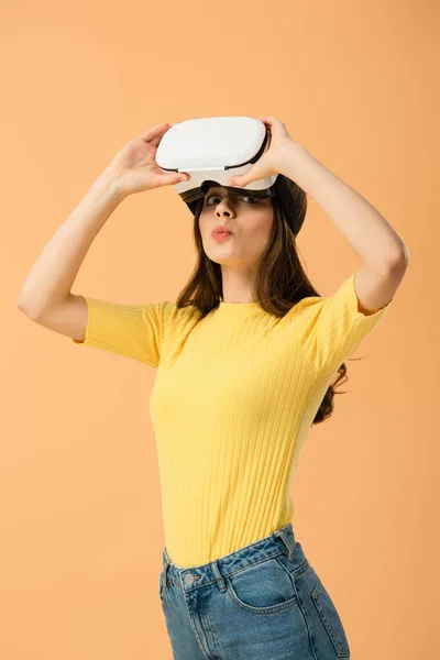 Amazed brunette girl touching vr headset and looking at camera isolated on orange — Stock Photo