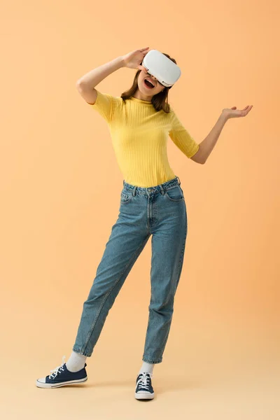 Pleine longueur vue de la femme brune en vr casque souriant sur fond orange — Photo de stock