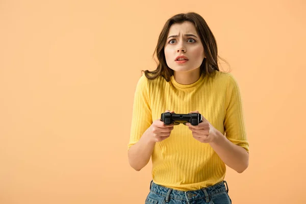 Verängstigte brünette junge Frau hält Gamepad isoliert auf orange — Stockfoto