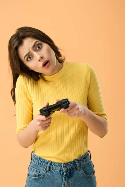 Schockierte brünette junge Frau hält Steuerknüppel isoliert auf orange — Stockfoto