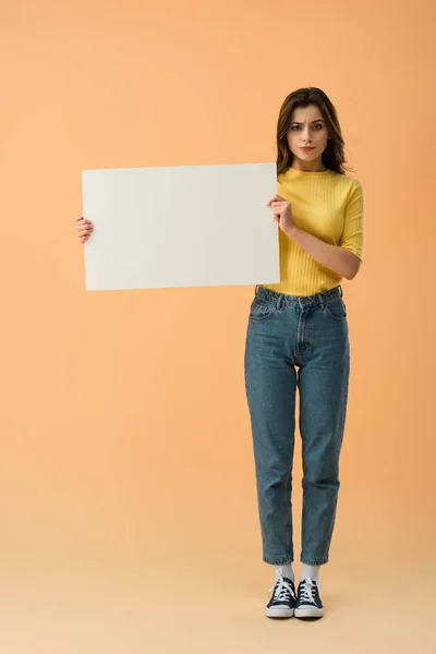 Пушистая брюнетка в джинсах и джинсах, держащая в руках бланк-карту на оранжевом фоне — стоковое фото