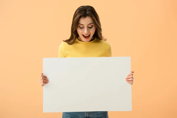 Aufgeregte brünette junge Frau hält leeres Plakat in der Hand und lacht isoliert auf orange — Stockfoto