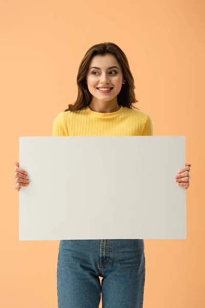 Blissful smiling brunette girl holding blank placard isolated on orange — Stock Photo