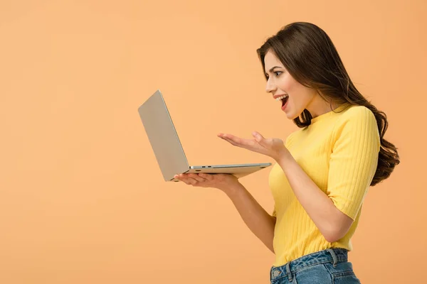 Emozionale bruna giovane donna che tiene il computer portatile isolato su arancione — Foto stock