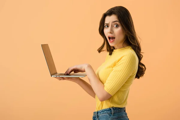 Shocked brunette young woman using laptop isolated on orange — Stock Photo